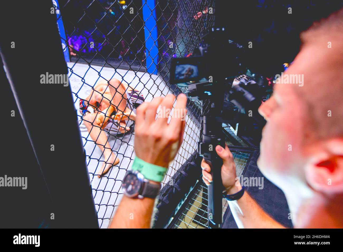 Professional cameraman, videographer is filming with camera for live broadcast MMA fighters as fight in fights without rules in the ring octagon Stock Photo