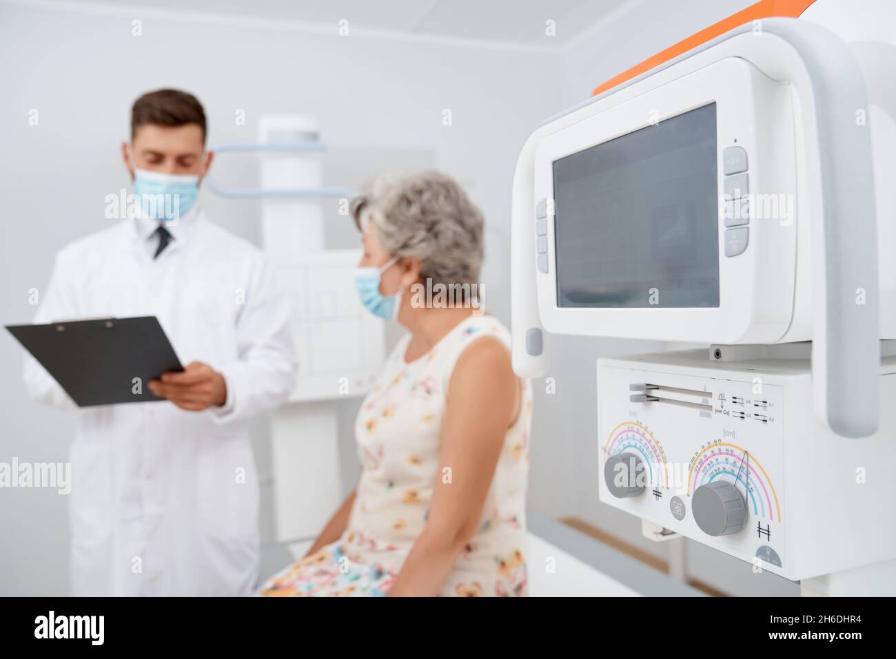 Close up of modern technology of ultrasound equipment foreground and patient with doctor on background. Brunette radiologist in white uniform reading diagnose and risk for old female patient. Stock Photo