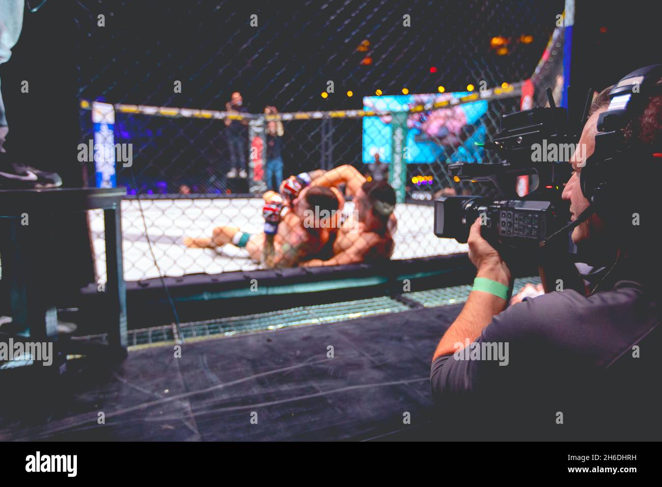 Professional cameraman, videographer is filming with camera for live broadcast MMA fighters as fight in fights without rules in the ring octagon Stock Photo