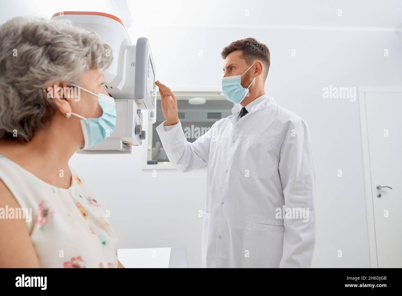 Side view professional radiologist touching screen of modern equipment starting scanning process. Old grey female patient waiting, examine health in modern clinic. Concept of medicine. Stock Photo