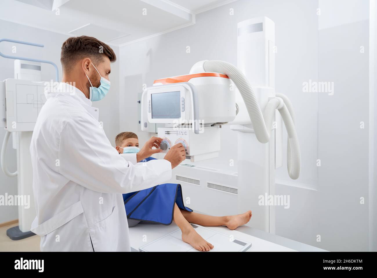 Side view of professional radiologist using moving modes equipment in clinic. Boy lie down in hospital on ultrasound diagnostic for leg after injury.Concept of kids medicine. Stock Photo