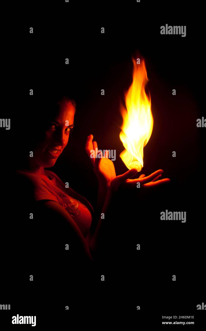 Woman holds fire in the palm of her hand looking at camera Stock Photo