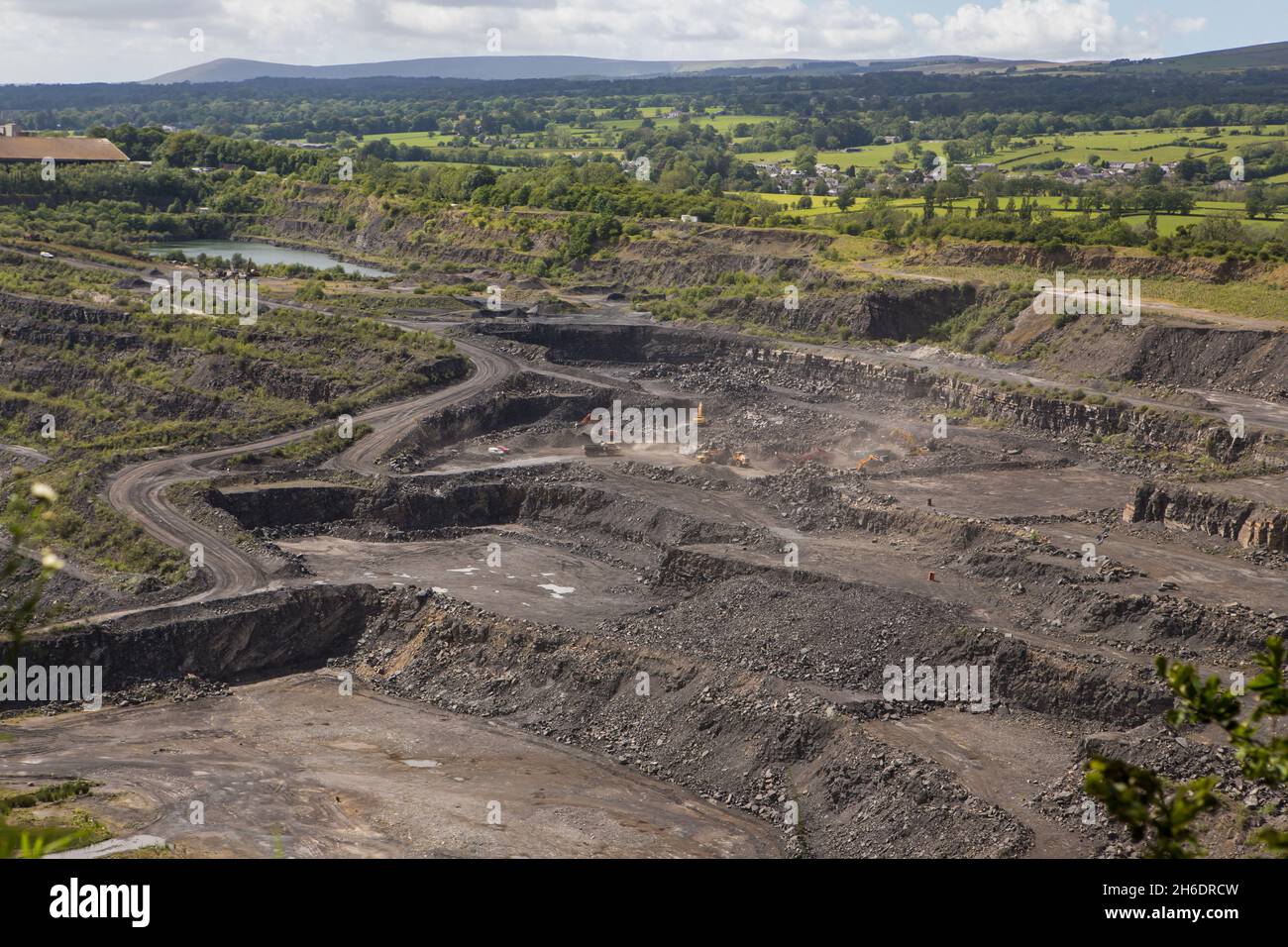 Large limestone quarry in Clitheroe, Ribble valley. Excavators and trucks working with rock terraces on the quarry walls Stock Photo