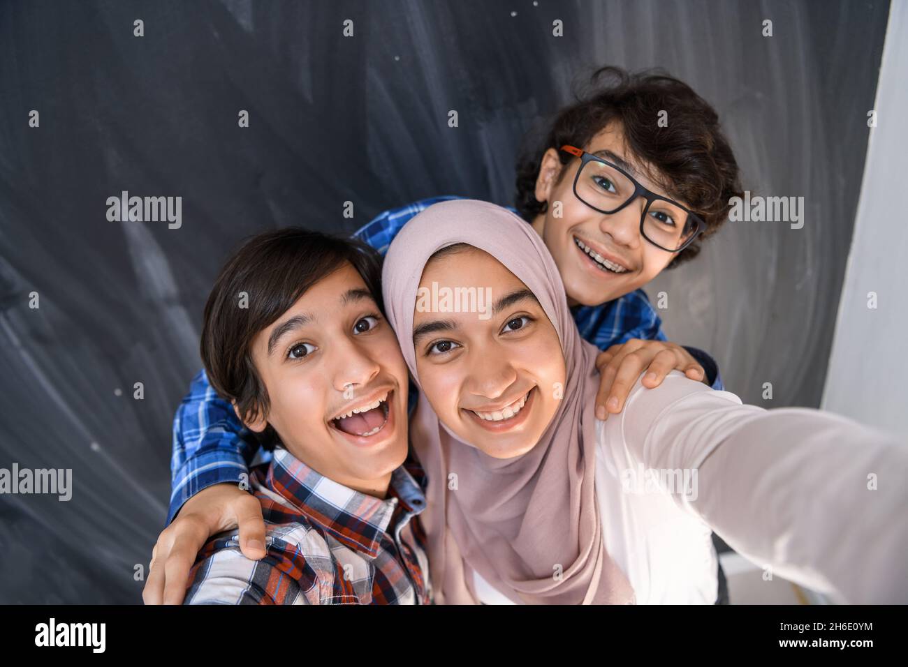 Group of arab teens taking selfie photo on smart phone with black chalkboard in background. Selective focus  Stock Photo