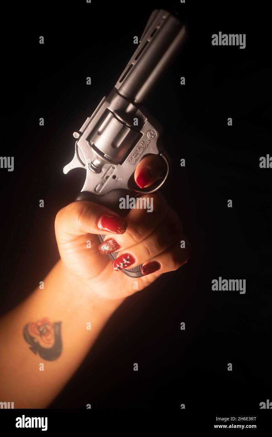Lady spy detective  with painted red nail varnish holding pistol gun at night Stock Photo