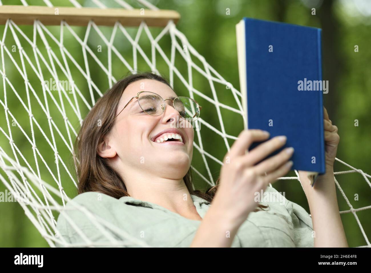 Happy woman with eyeglasses reading a book on a hammock in a forest Stock Photo