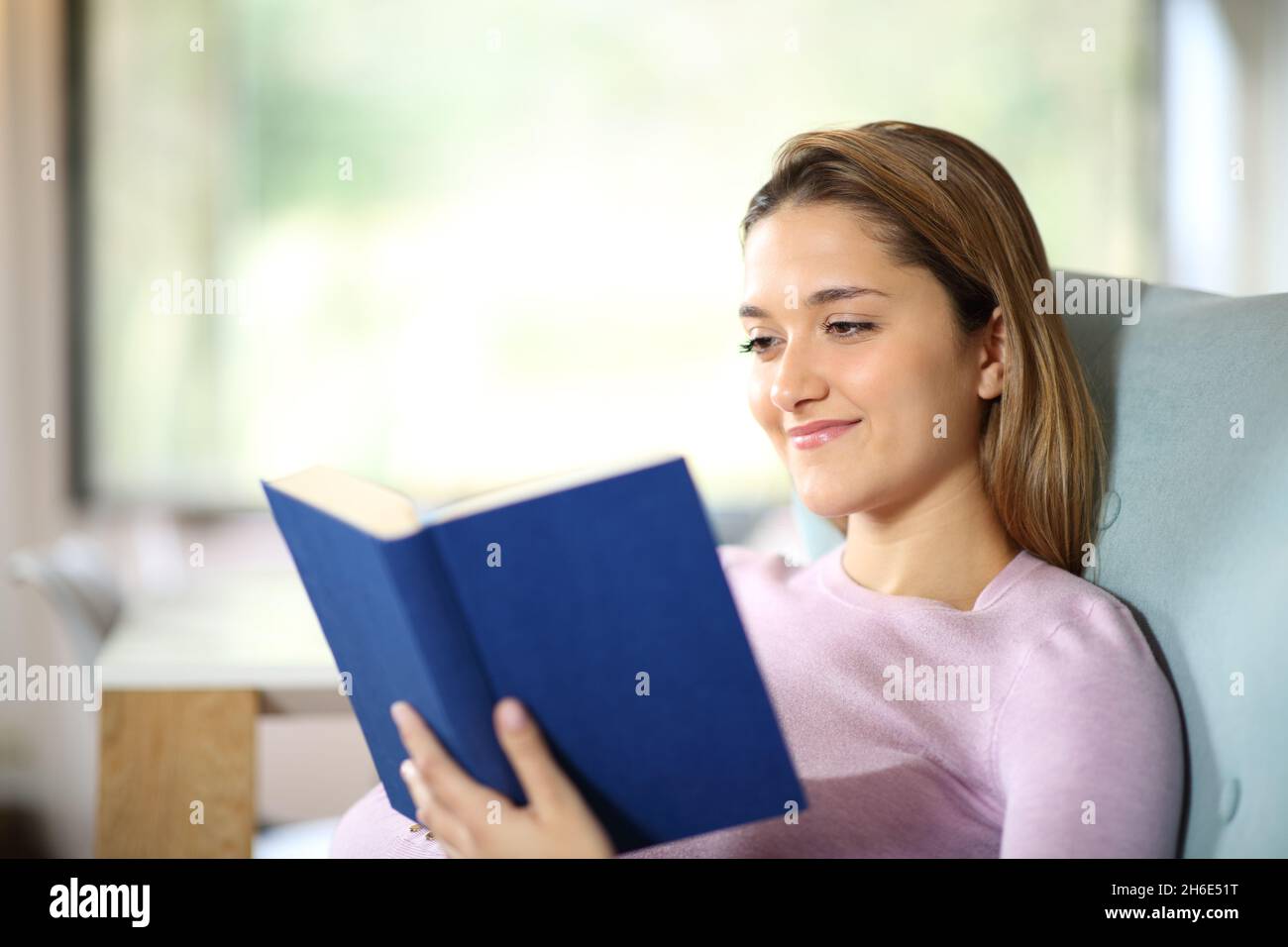 Happy woman sitting on a couch at home reading a paper book Stock Photo