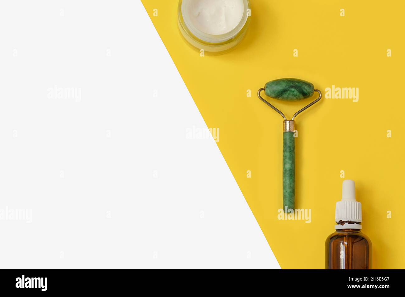 Creative composition with jade roller, face cream, serum on two color yellow and white background with space for text Stock Photo
