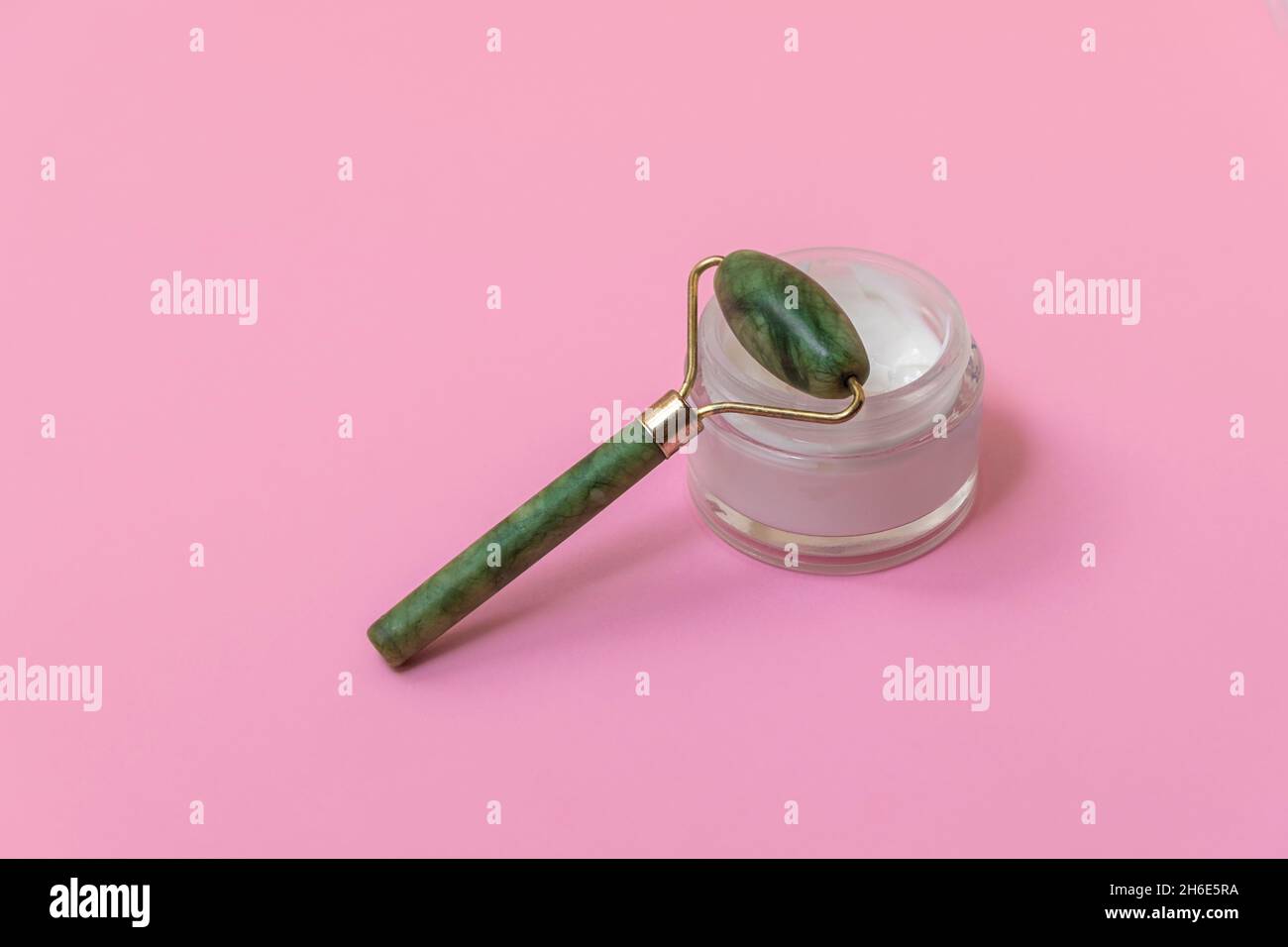Green jade face roller for anti-age skincare on soft pink background with copy space Stock Photo