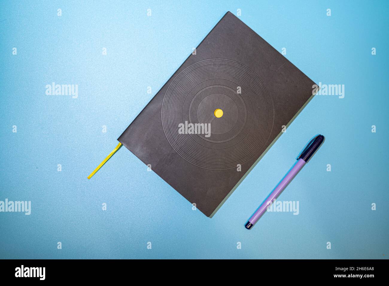 Black notebook with purple pen on blue background Stock Photo