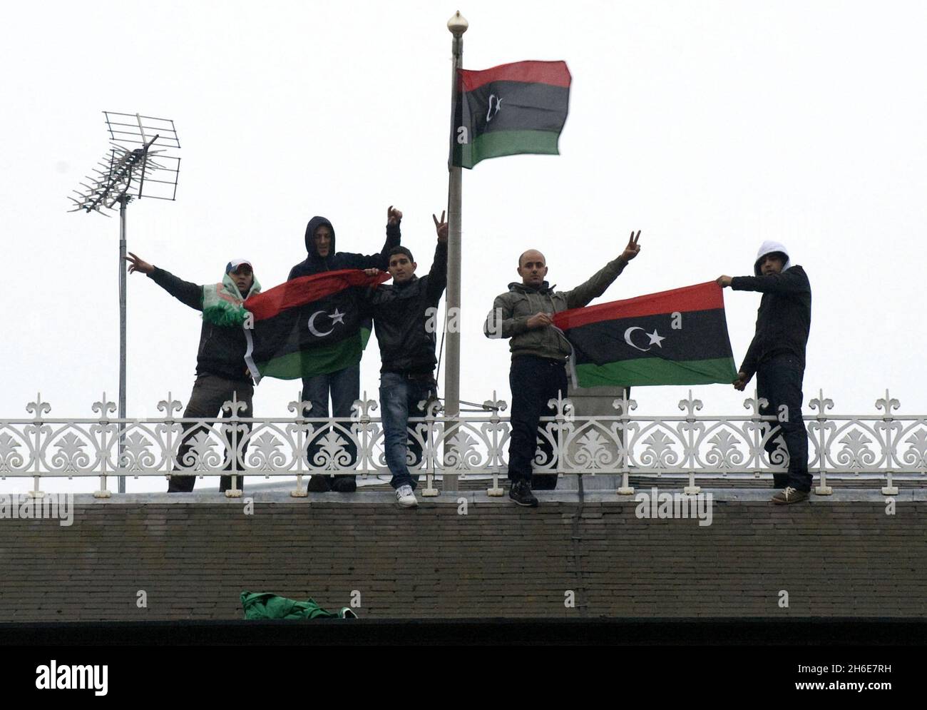 Protesters climb onto the roof of the Libyan embassy in central London to demonstrate against Moamer Kadhafi's regime, replacing the national flag with one used by Libyan rebels. Five young men made victory signs and held up the Libyan monarchist flag, a black, red and green standard with a crescent and star which Kadhafi has banned for more than 40 years. Stock Photo