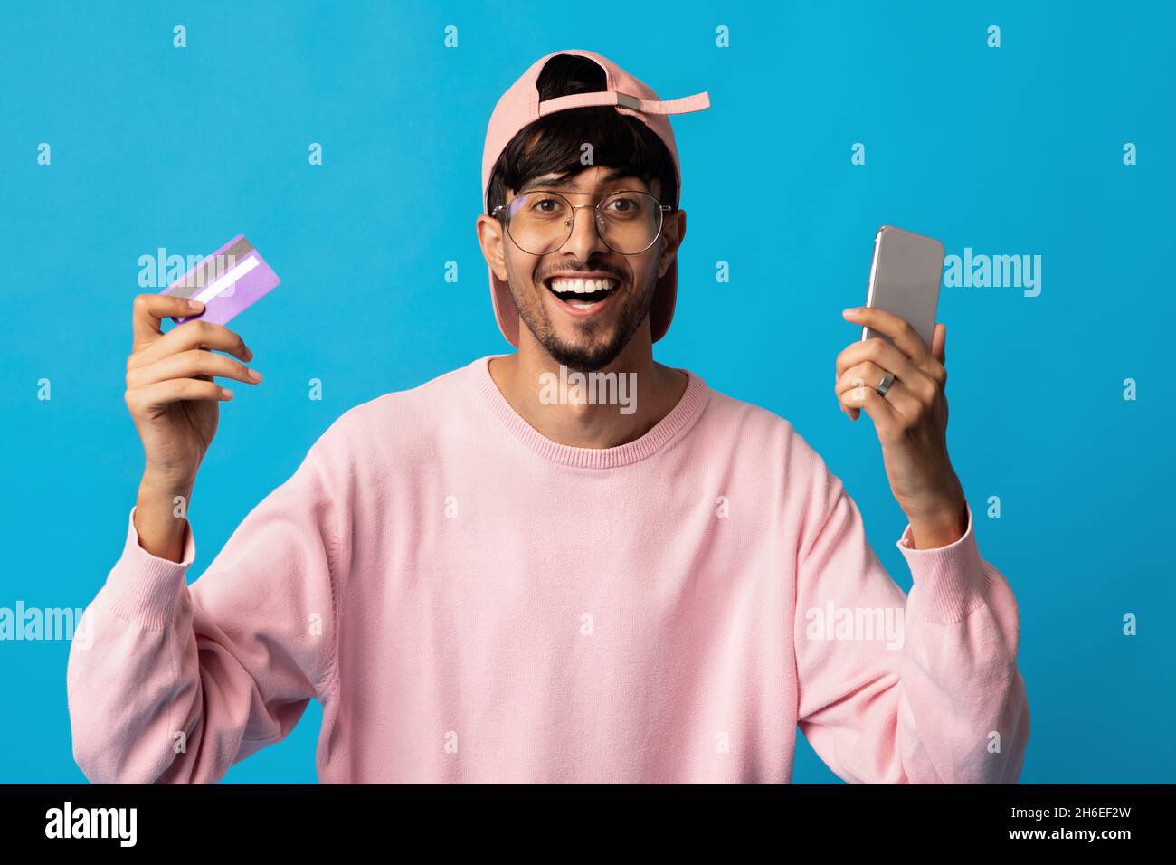 Emotional indian guy holding smartphone and credit card Stock Photo - Alamy