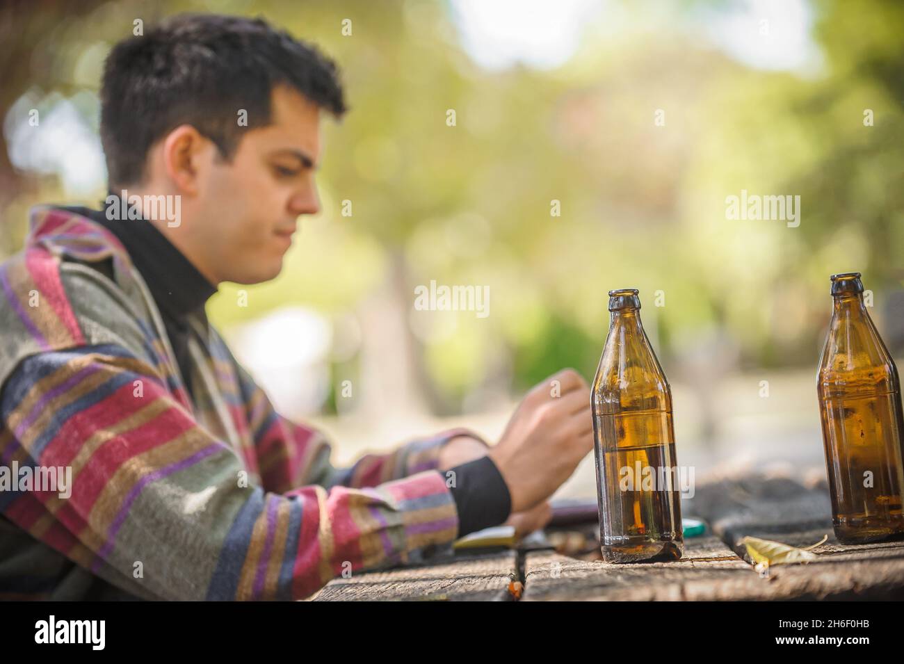 Lonely man drinks beer from bottle alone and thinks about the meaning of  life. Wooden bench with table in forest park outdoor. Real life scene Stock  Photo - Alamy