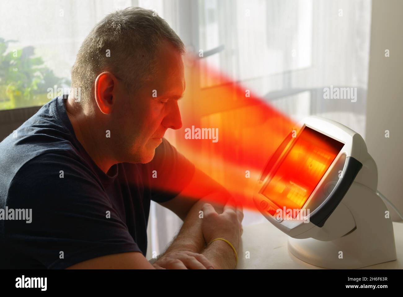 Man treating pain in the sinuses and head with infrared light therapy. The man sits at the table near the healing lamp. Stock Photo