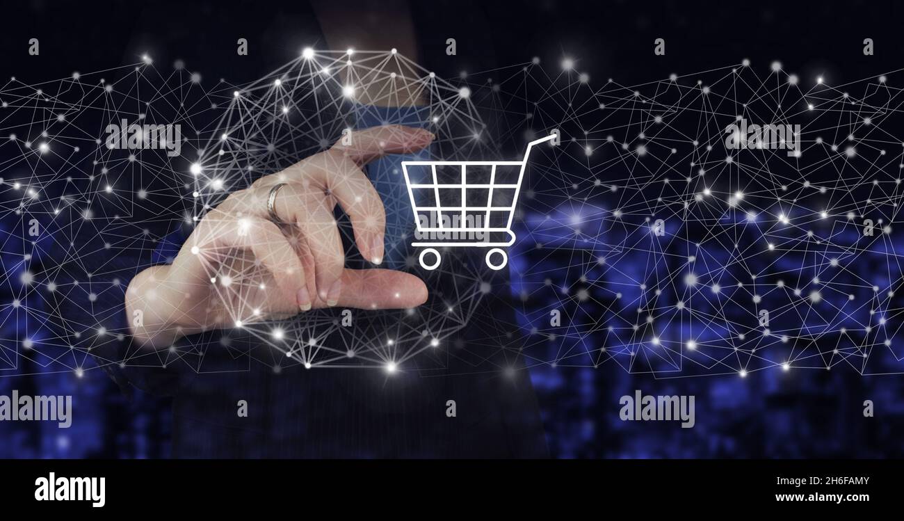 Internet Cart Web Store Online Buy E-Commerce concept. Hand hold digital hologram cart sign on city dark blurred background. Online shopping or intern Stock Photo