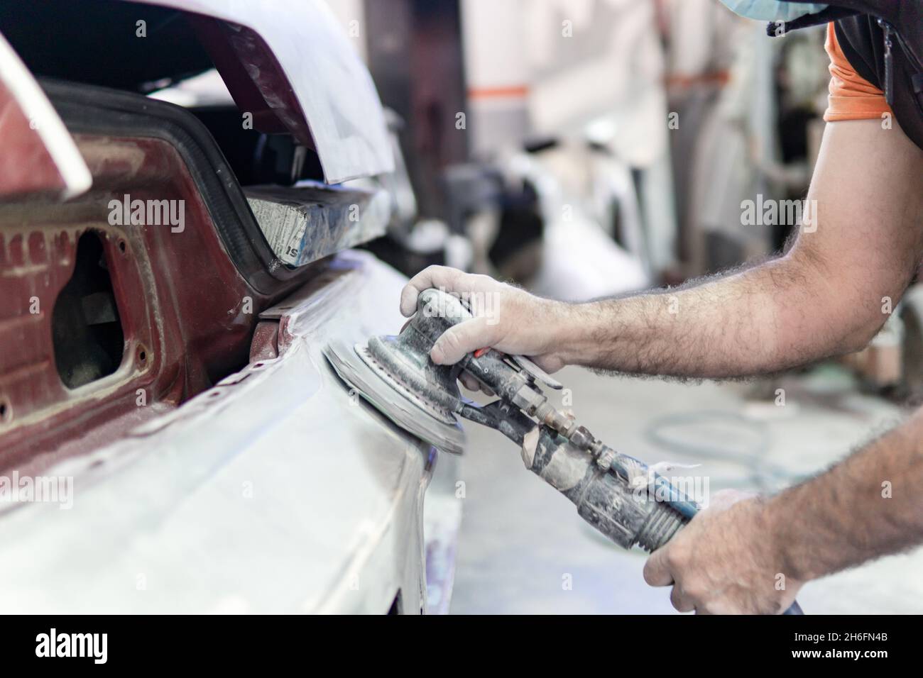 Side view Auto mechanic sanding a part of a car in a garage. Pre Stock