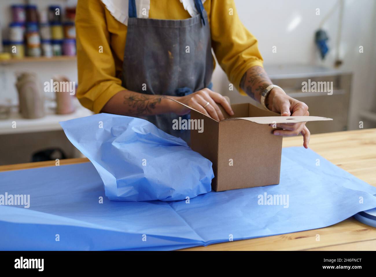 Woman ceramist packing crockery in box for delivery. Female wrap