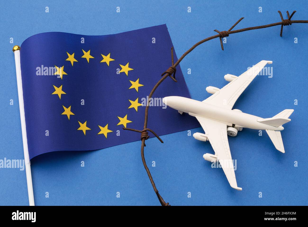 EU flag, barbed wire and toy plane on blue background, european union closed air border concept