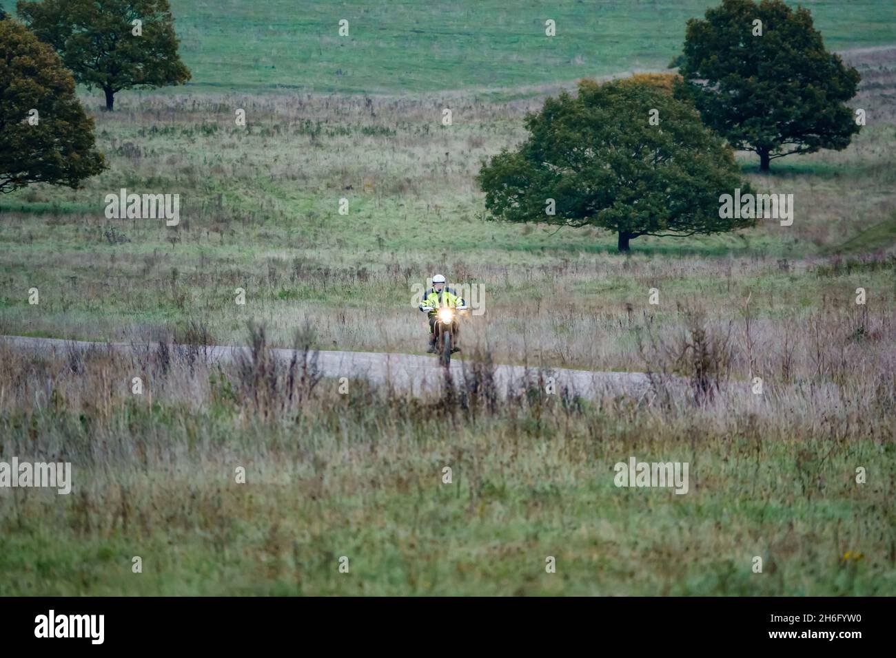 a motorcyclist (biker) in a hi-vis yellow jacket riding his motorbike along a stone track on Salisbury Plain, Wiltshire Stock Photo