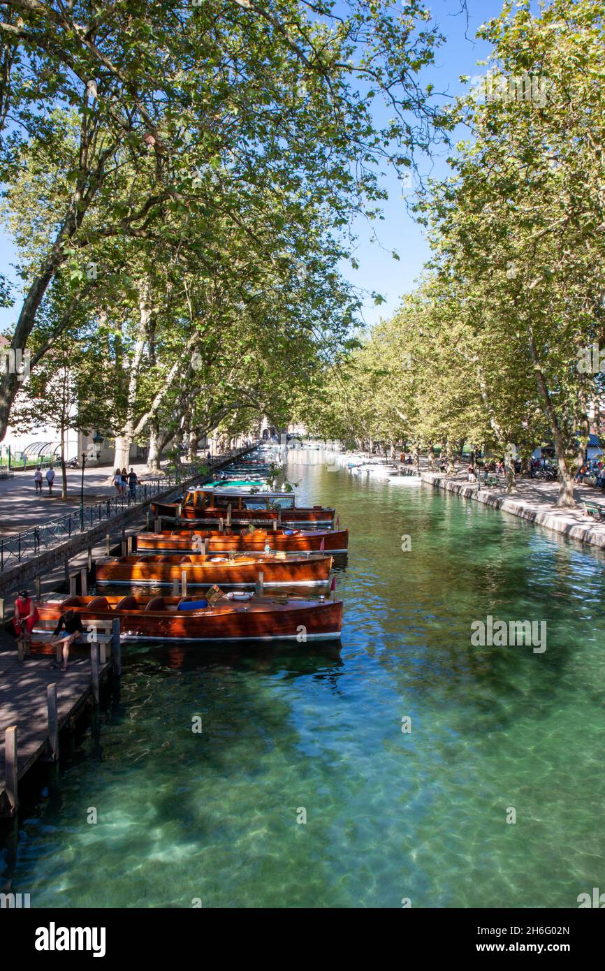 A tranquil scene with row of boats on a canal lined by trees on a summers day, in Annecy, France Stock Photo