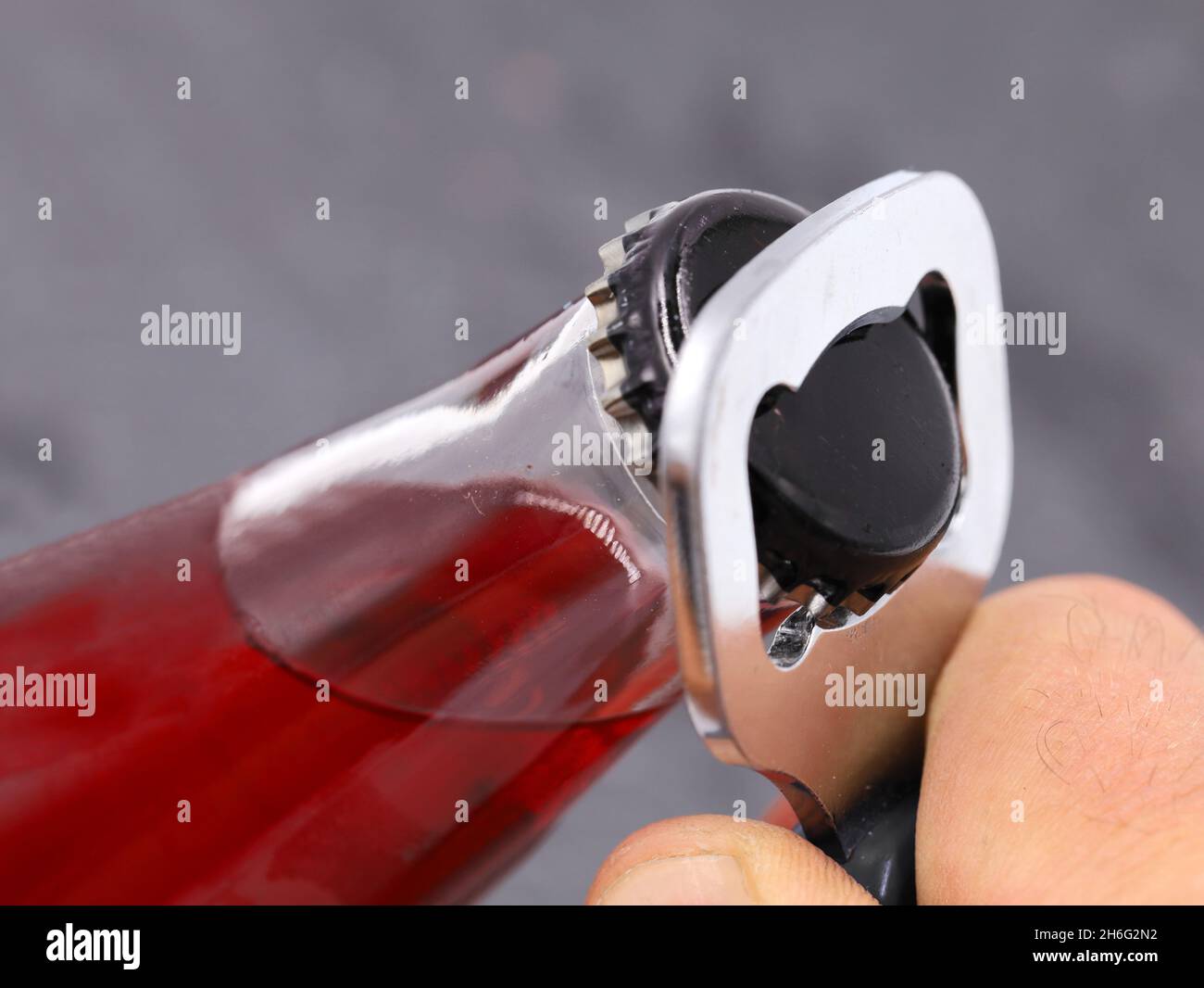 opening red drink bottle with bottle opener on grey background, close up Stock Photo