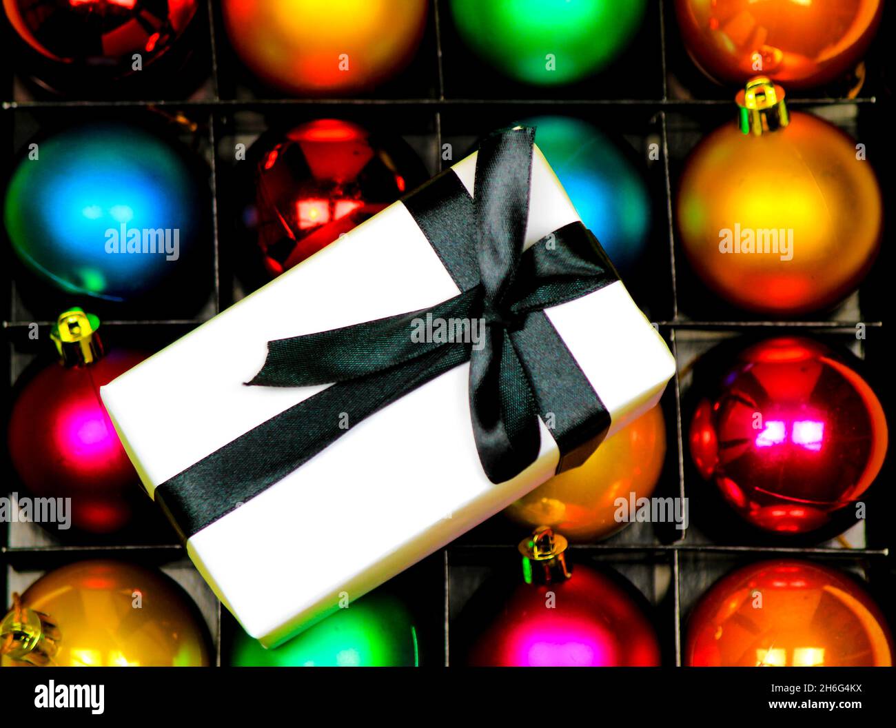 Gift wrapped with white paper and black bow on multicolor Christmas balls Stock Photo