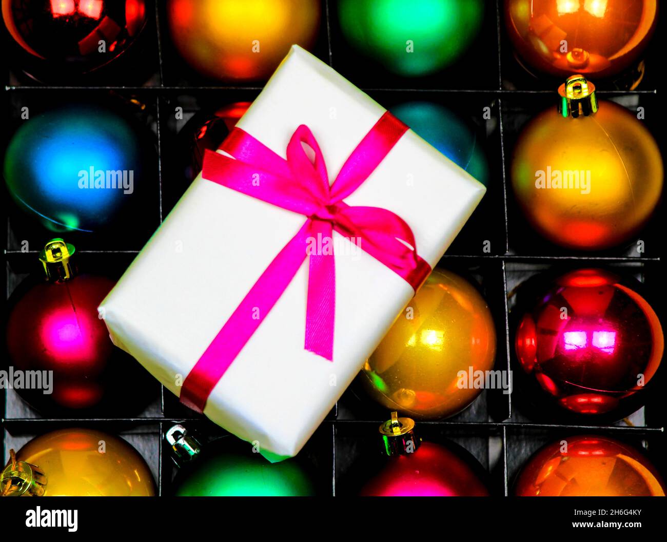 Gift wrapped with white paper and pink bow on multicolor Christmas balls Stock Photo