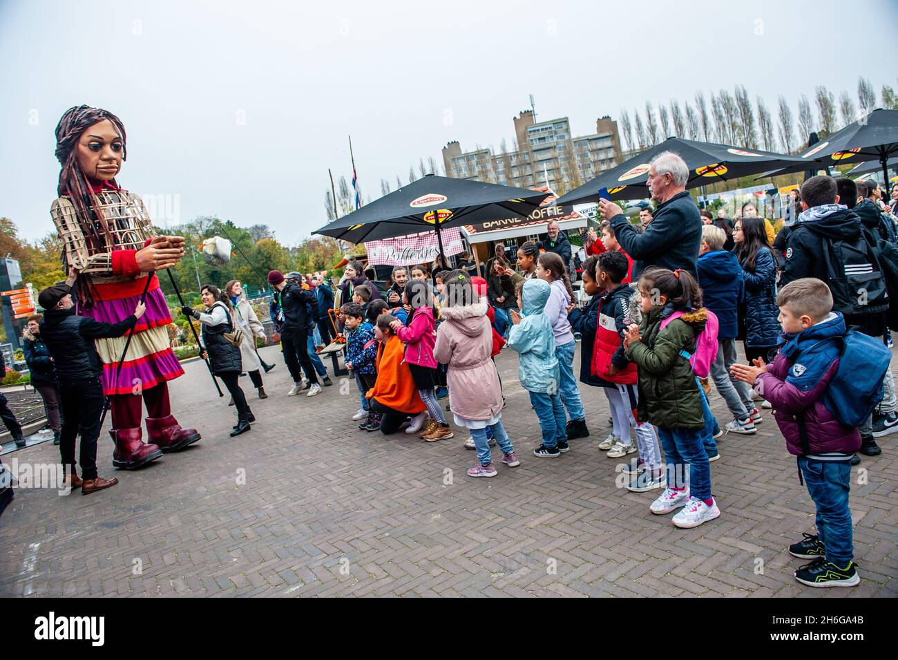 A group of children seen dancing with Little Amal.Amare, a new cultural hub in the center of The Hague has organized as a part of its 'Open Festival', the visit of the giant puppet 'Little Amal', a nine-year-old Syrian refugee girl and over 11-feet-tall to the miniature park, Madurodam. She is invited to take part in the Festival as a special guest in the city to grab attention across Europe to the plight of young refugees who have fled from Syria. Amal was received outside the park by a group of children, after that she could walk around the 1:25 scale model replicas of famous Dutch landmarks Stock Photo