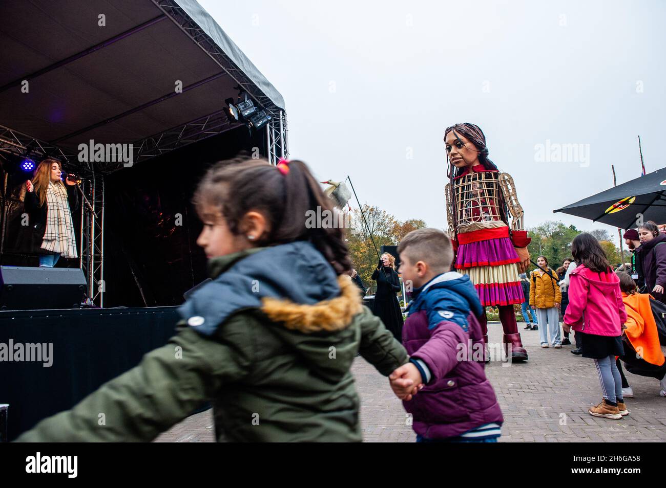 Children are seen dancing around Little Amal.Amare, a new cultural hub in the center of The Hague has organized as a part of its 'Open Festival', the visit of the giant puppet 'Little Amal', a nine-year-old Syrian refugee girl and over 11-feet-tall to the miniature park, Madurodam. She is invited to take part in the Festival as a special guest in the city to grab attention across Europe to the plight of young refugees who have fled from Syria. Amal was received outside the park by a group of children, after that she could walk around the 1:25 scale model replicas of famous Dutch landmarks, and Stock Photo