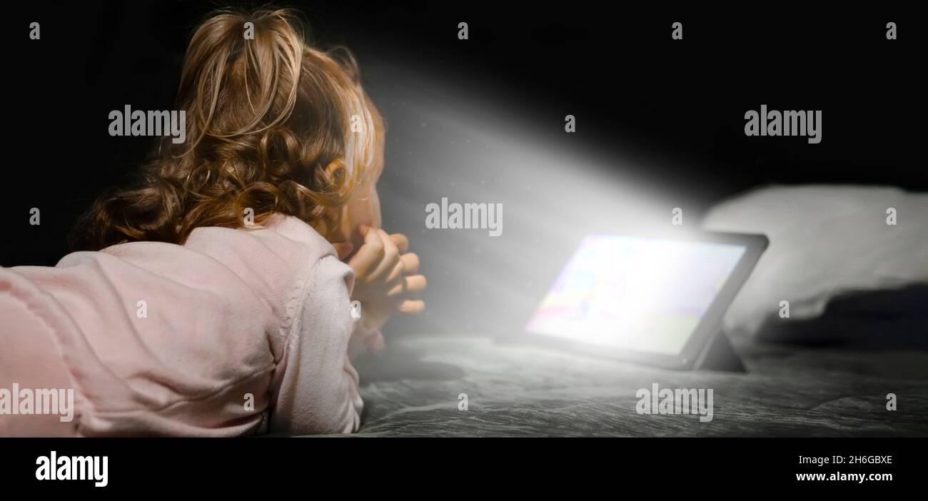 A little child watching animations very close to a bright tablet screen. Concept of harmful habits, screen time, and bad parenting Stock Photo