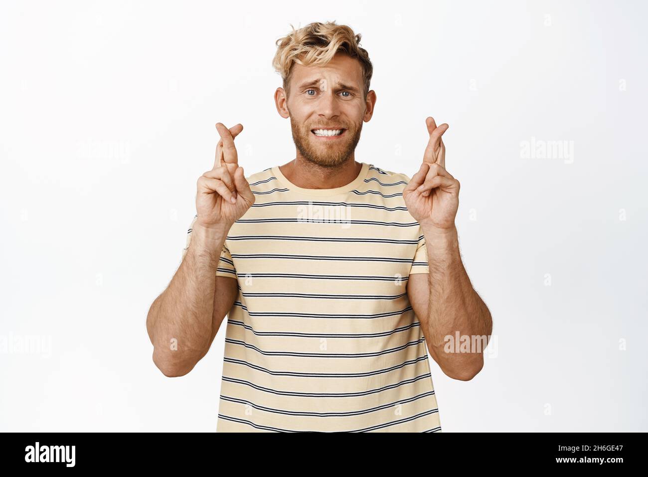 Portrait of adult man looking hopeful, praying with fingers crossed
