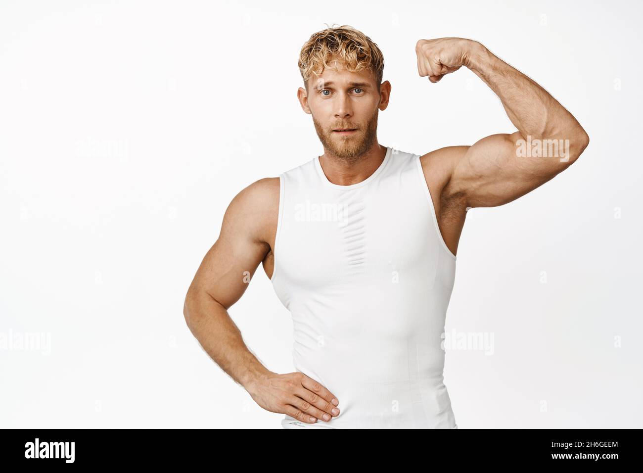Portrait of strong and handsome young athlete showing his muscle on arm, flexing biceps and looking confident, white background Stock Photo