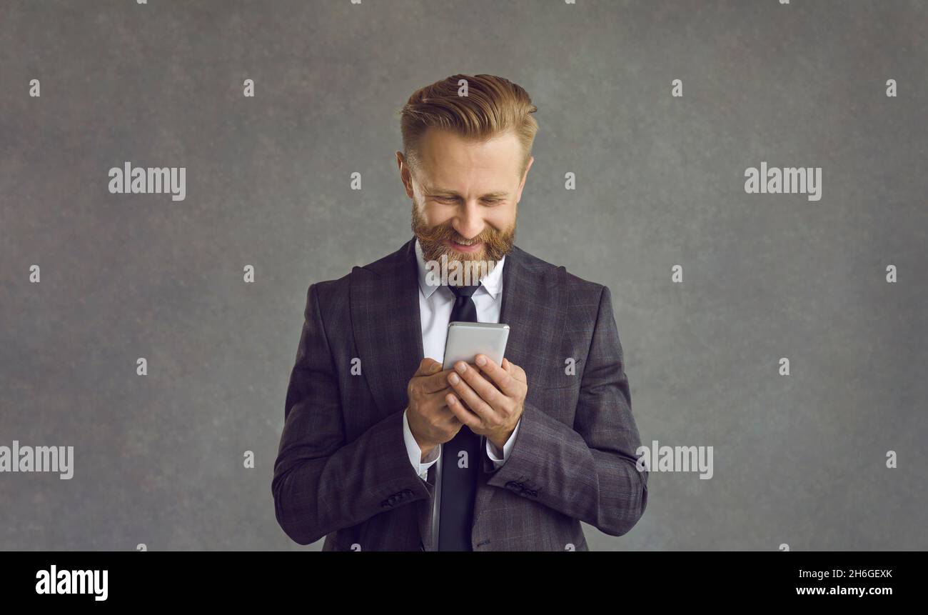 Smiling businessman using smartphone standing over grey studio background Stock Photo