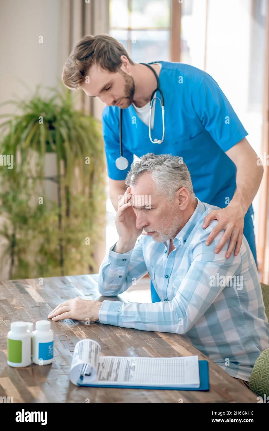 Attentive doctor supporting a depressed gray-haired man Stock Photo