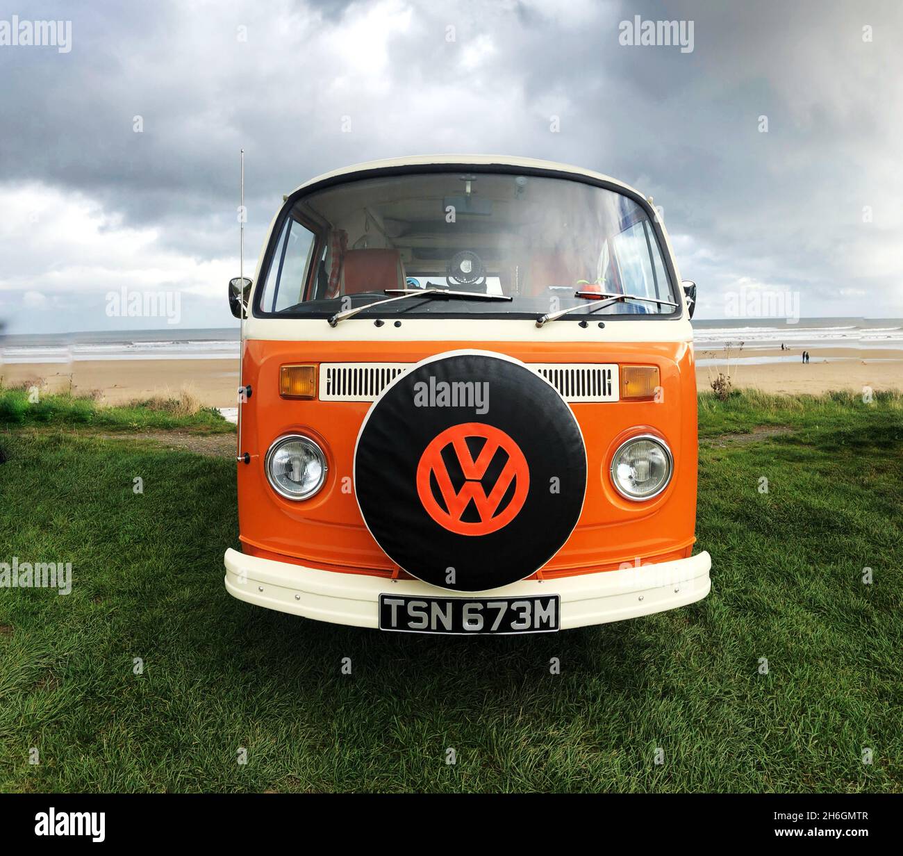 A front view of a classic Volkswagen Orange campervan at the beach with the VW badge on the vehicle tyre cover Stock Photo