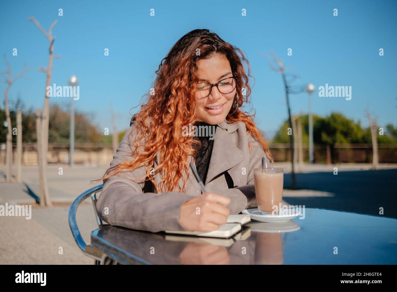 beautiful latin girl drinking a cup of coffee and watching the mobile phone, on a metal table outdoors Stock Photo