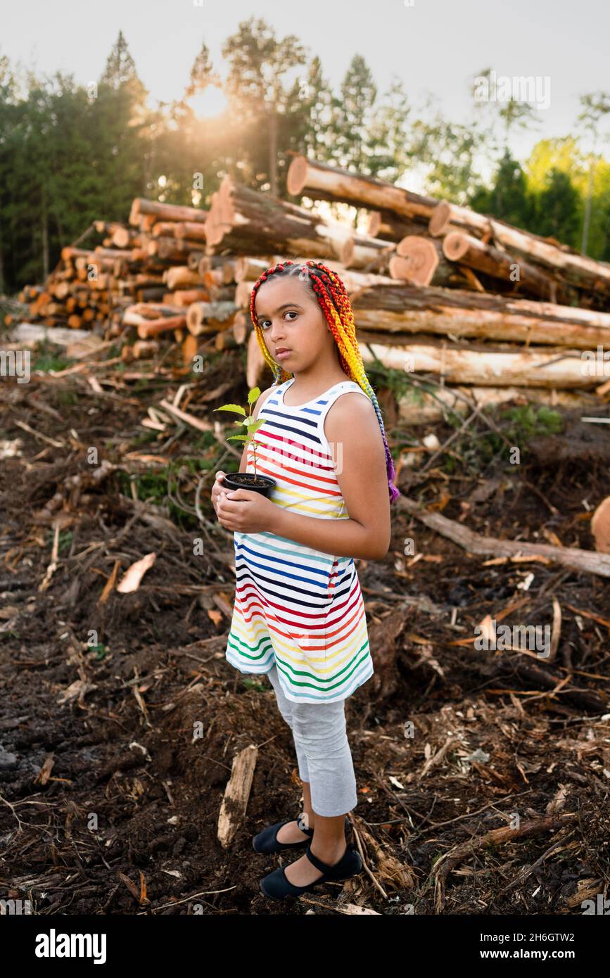 Young mixed race girl with rainbow box braids stands on logging site