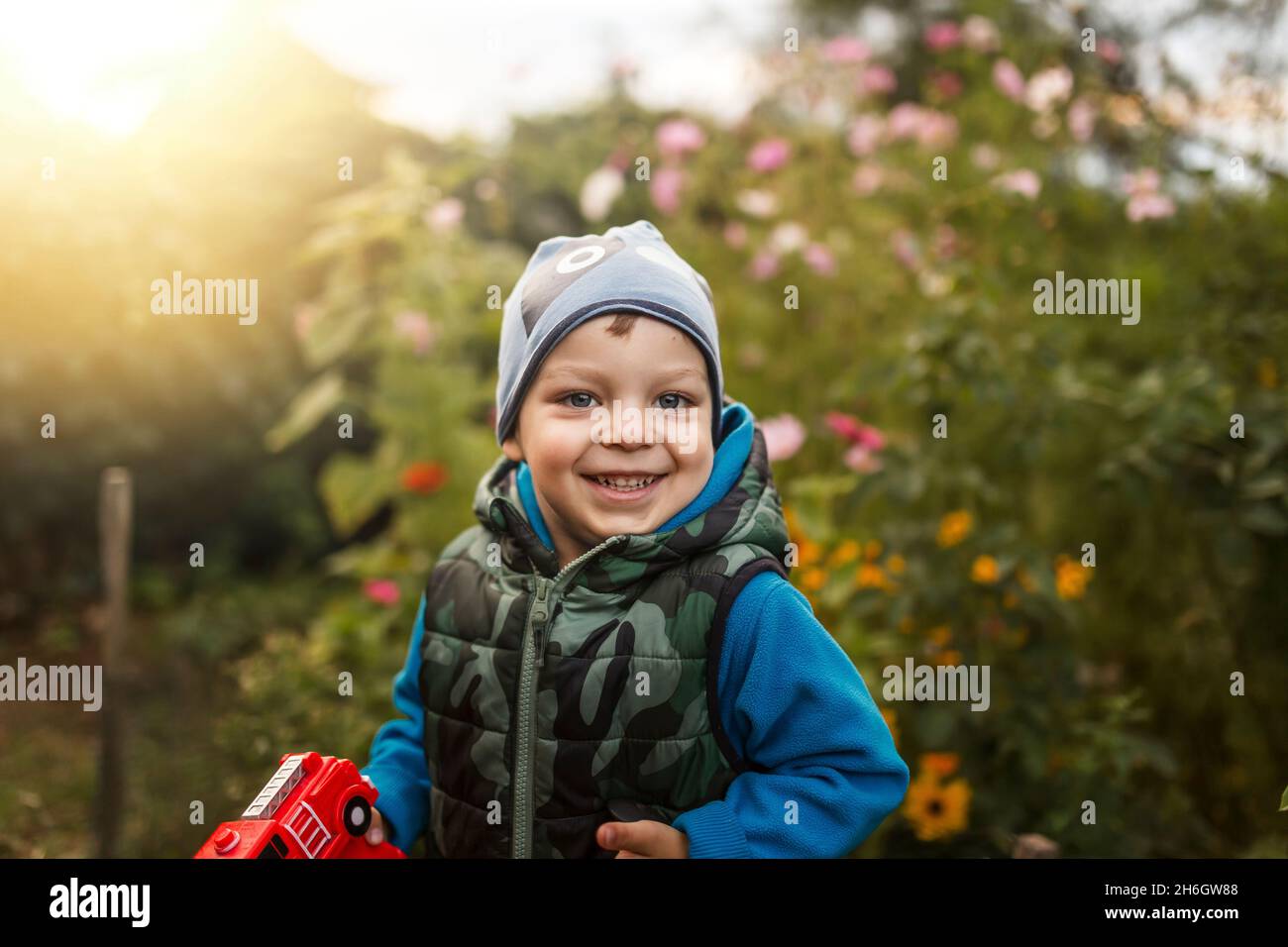 Toddler boy smiling in garden full of flowers wearing blue clothes Stock Photo