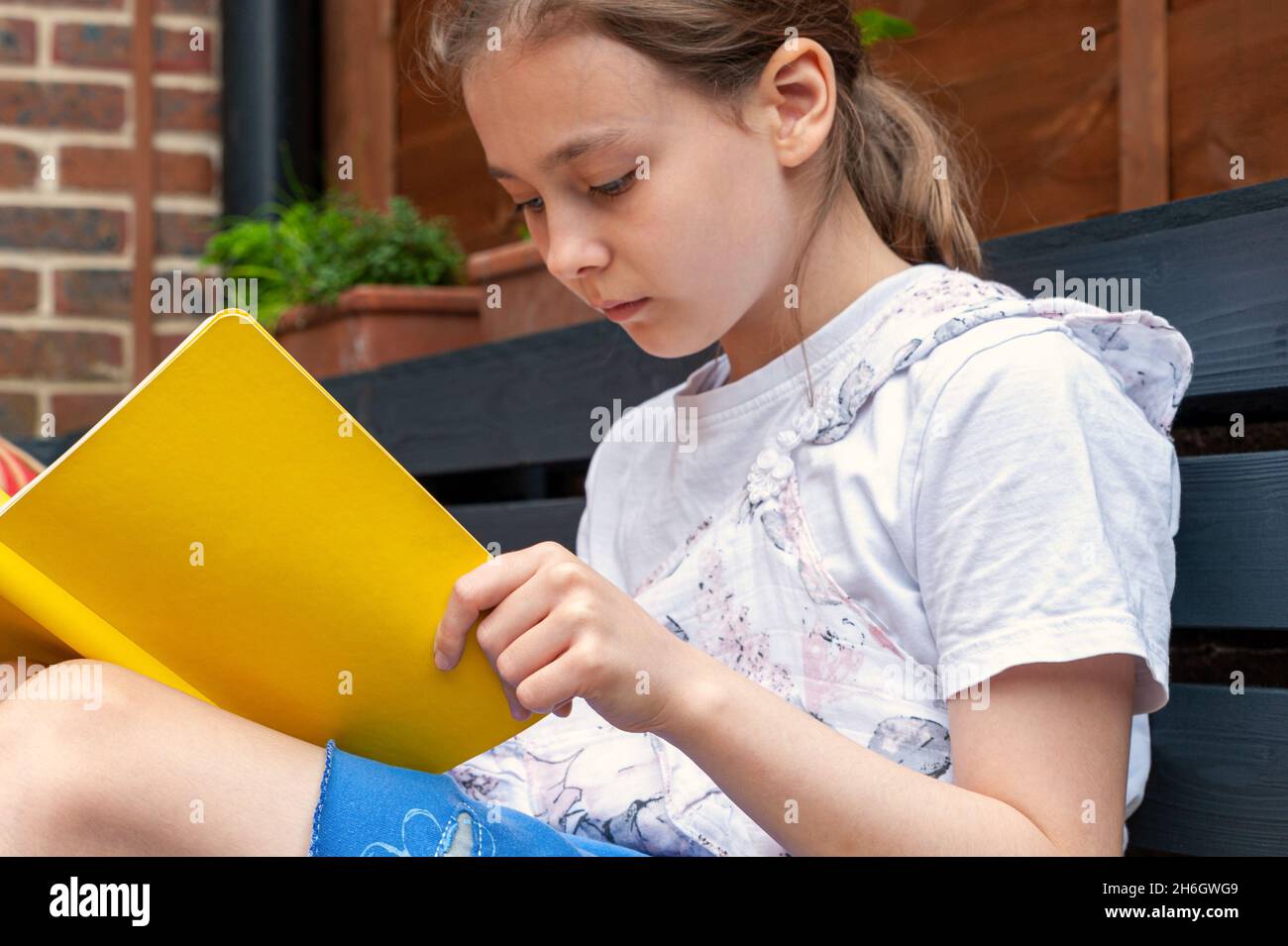 School age girl sitting in garden and doing prep work for her school. Stock Photo