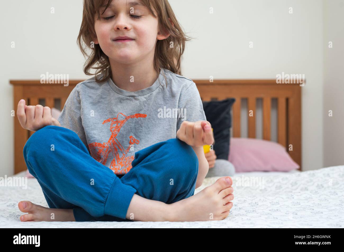Cute, little boy sitting comfortably on bed in bedroom and training yoga in lotus pose Stock