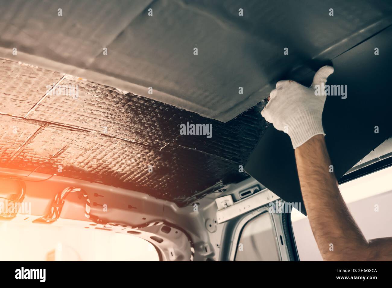 Worker hands glues soundproofing material to inside of car roof