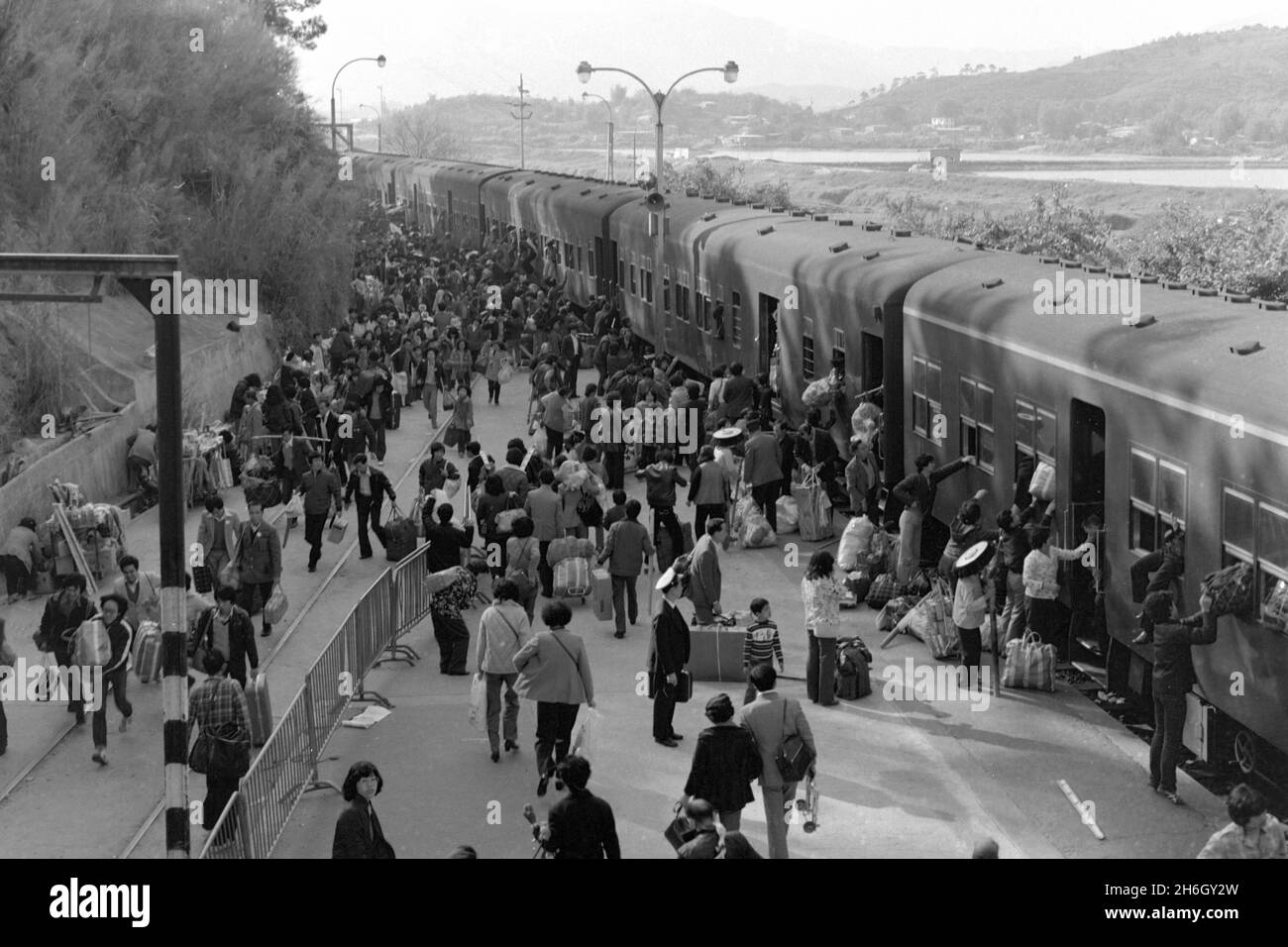 Lo Wu Railway Station, Hong Kong. View from Station Roof - looking south - of passengers getting off a train, heading back to Mainland China at Lunar New Year, 1981. Many are carrying presents for relatives, using bamboo yokes to balance their parcels. The diesel trains were phased out when the Kowloon-Canton Railway (HK section) was electrified in the early 1980s Stock Photo