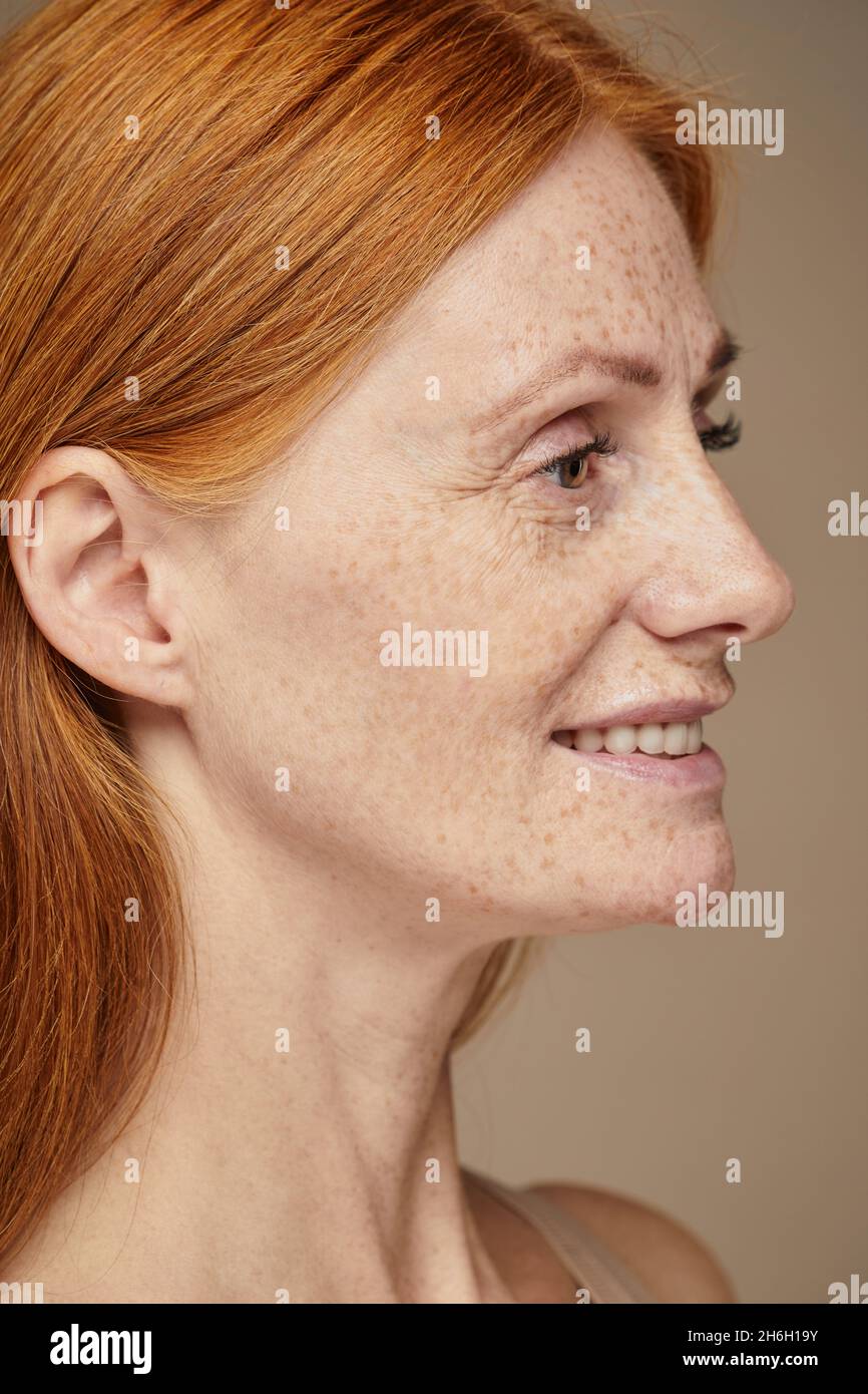 Vertical profile view portrait of beautiful red haired woman with freckles smiling Stock Photo
