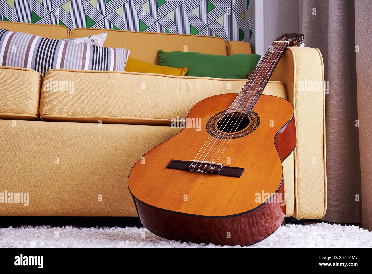 Old classic guitar in the interior close to the soft elegant yellow sofa. Musical instruments in interior and design Stock Photo