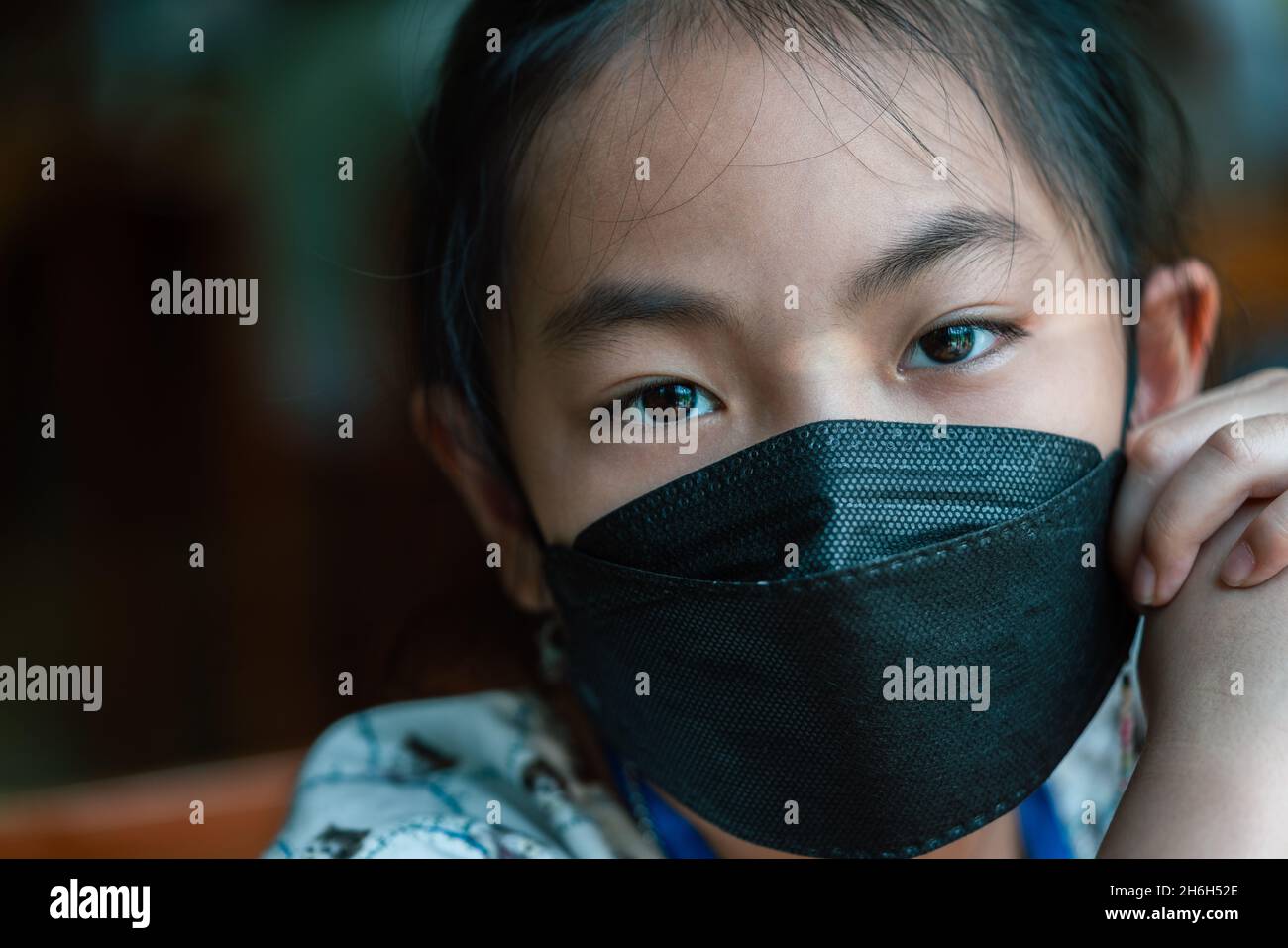 Close-up face of Asian child girl at 8 years old wearing medical black color mark, emotional eyes look at the camera. Stock Photo