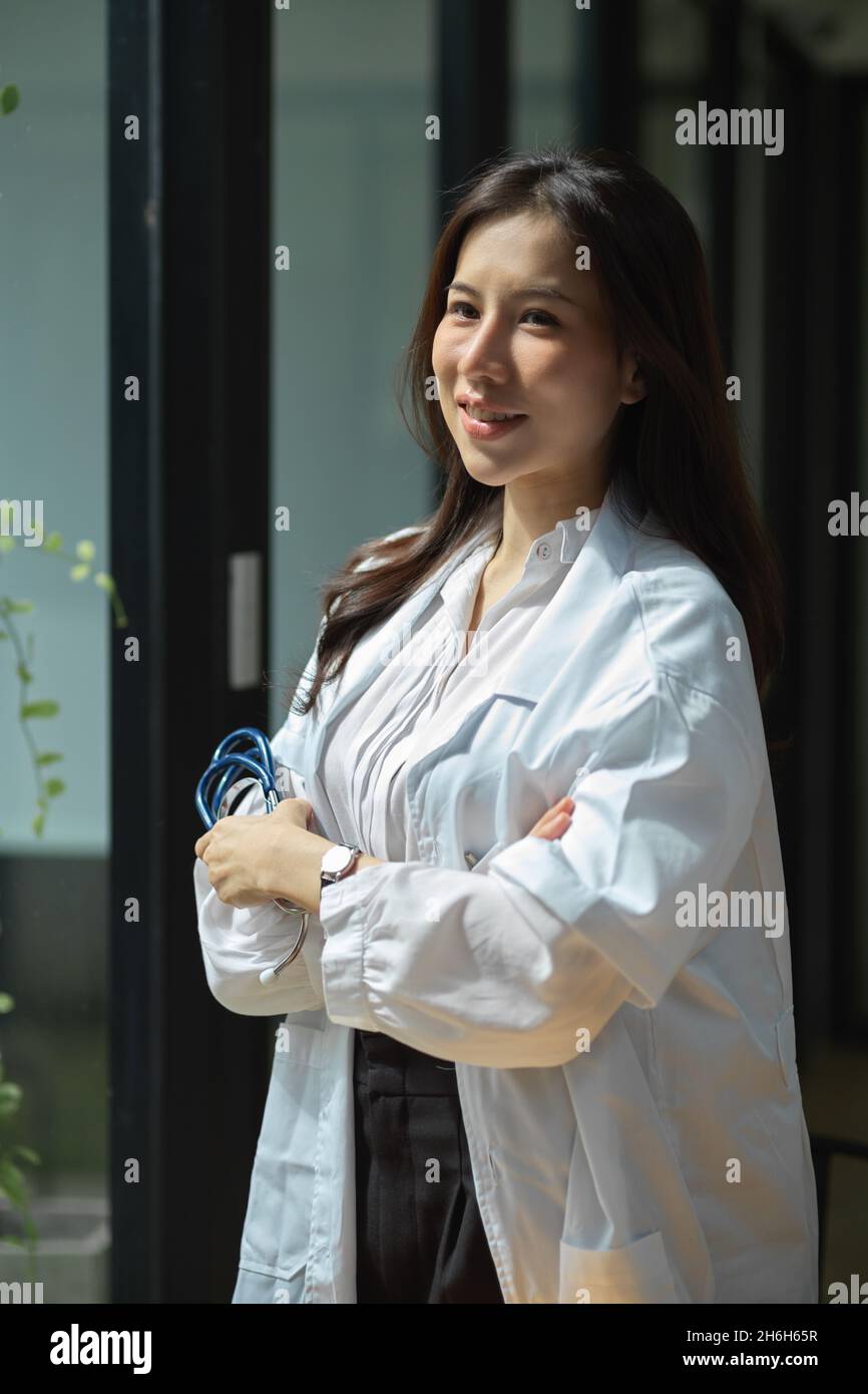 A confident young Asian female doctor in a medical white gown stand in ...
