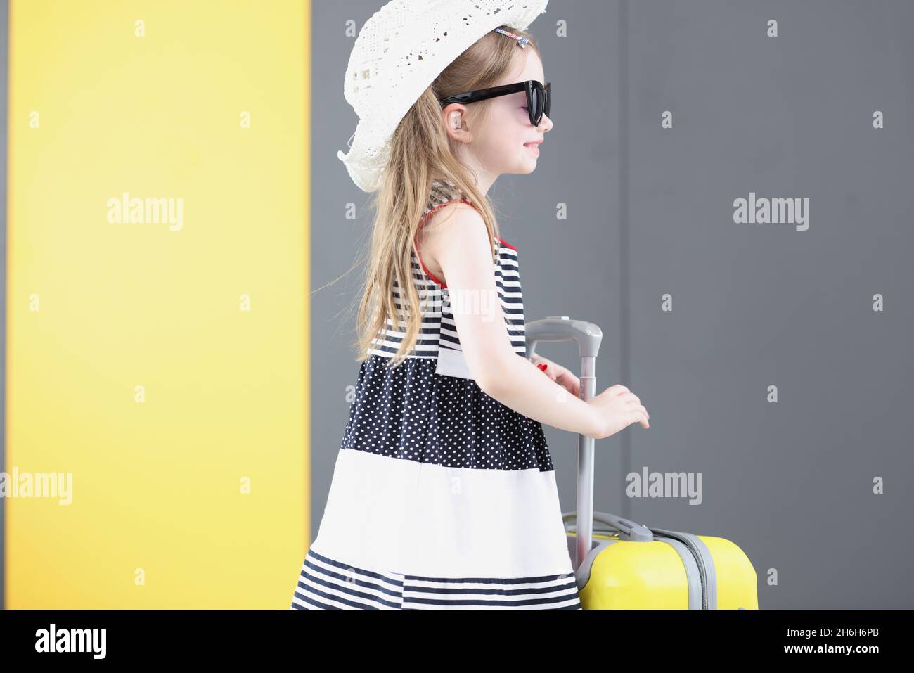 Well dressed little girl going on vacation carry yellow suitcase with her Stock Photo