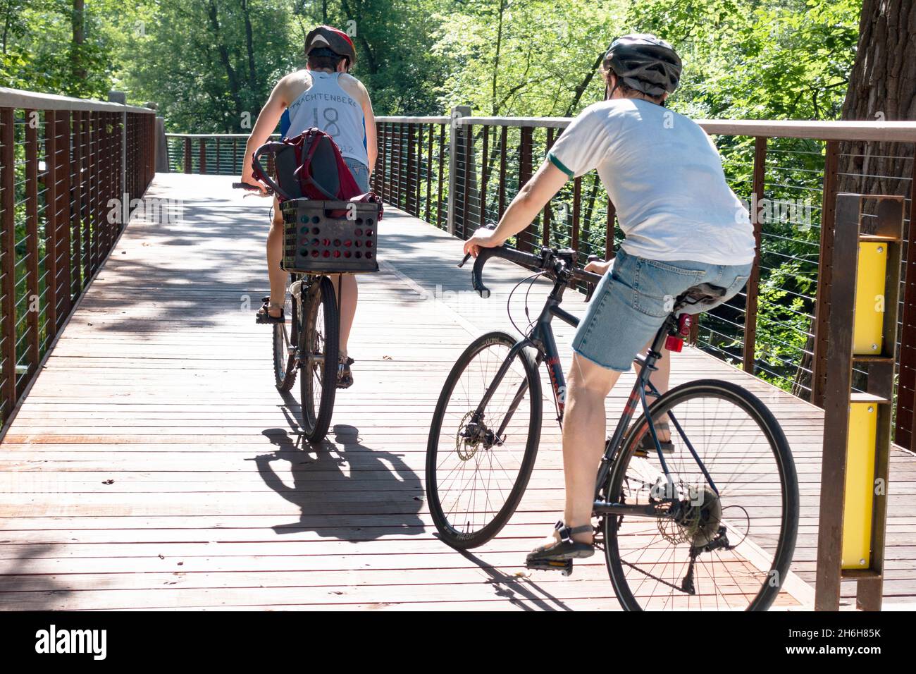 Two women bicycling on a wooden bridge on the Minnehaha Creek pathway. Minneapolis Minnesota MN USA Stock Photo