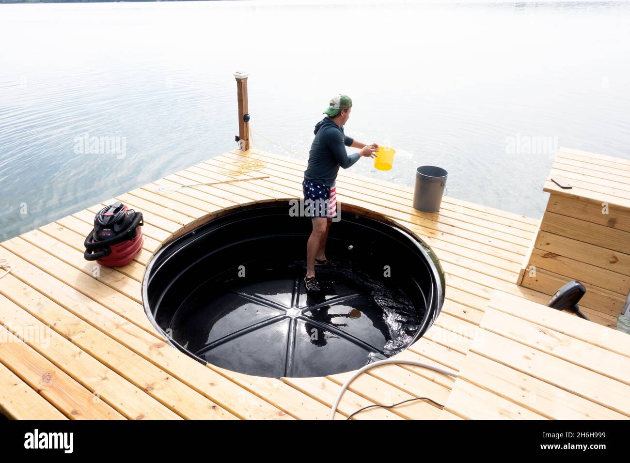 young man bailing out the  hot tub on a boat which he built wearing patriotic shorts. Clitherall Minnesota MN USA Stock Photo