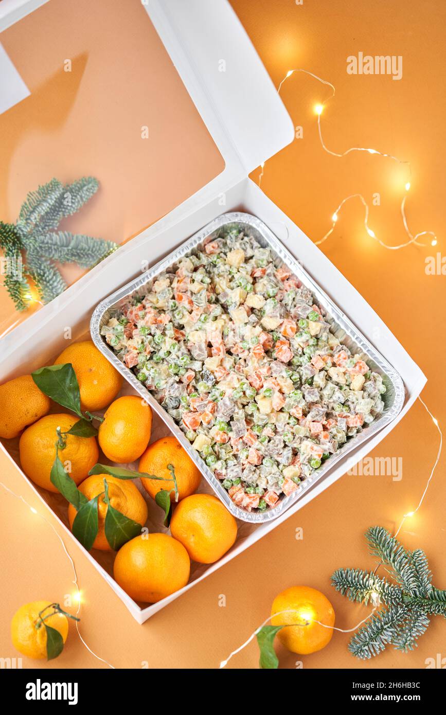 Traditional New Year and Christmas salad on holiday, in take way box. Menu food for delivery in the Coronavirus Pandemic. Tangerines and branches of t Stock Photo